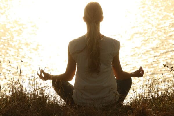 A woman sitting in the grass doing yoga.