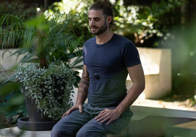 A man sitting on the ground in front of some plants.