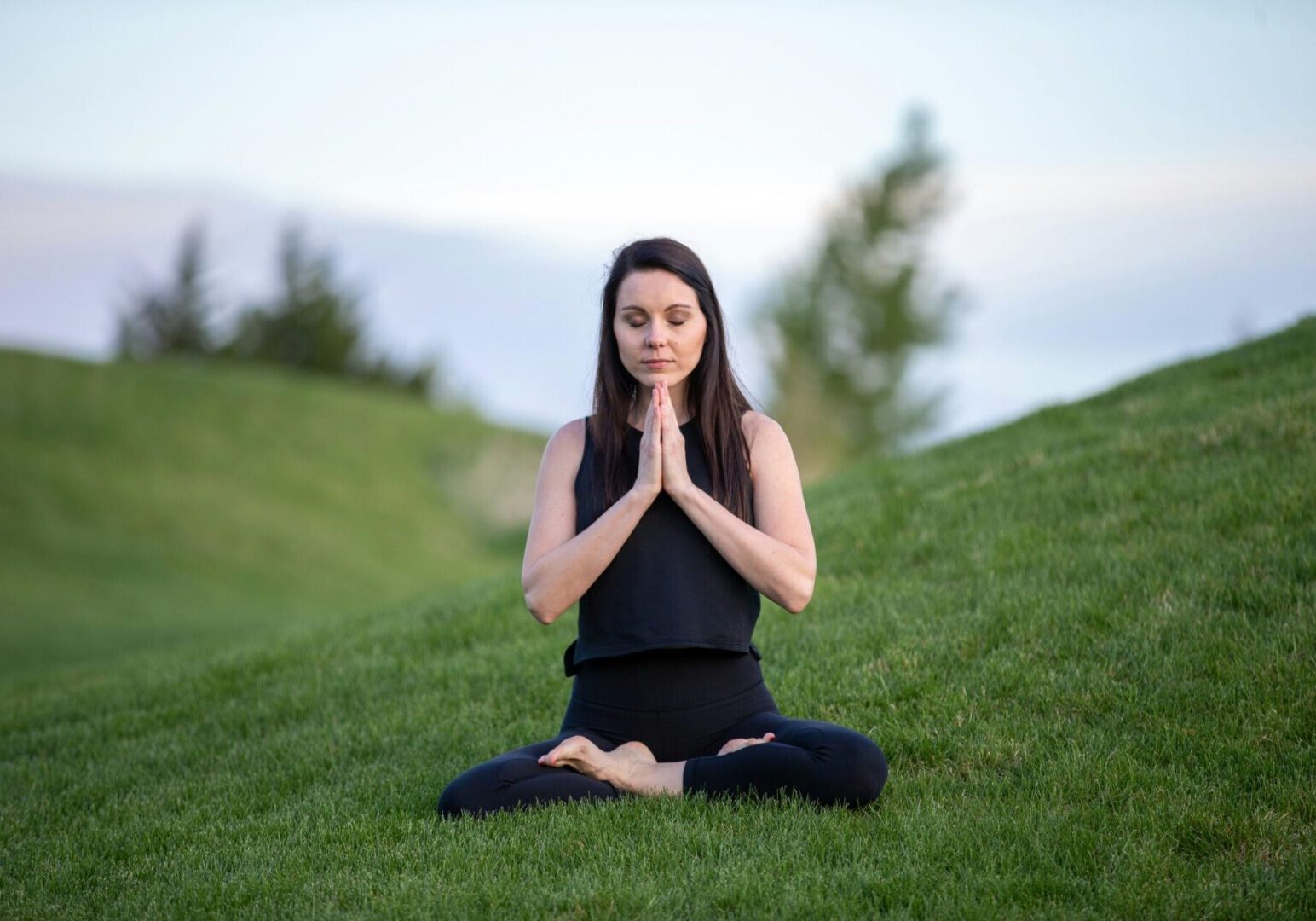 A woman sitting in the grass with her hands folded together.